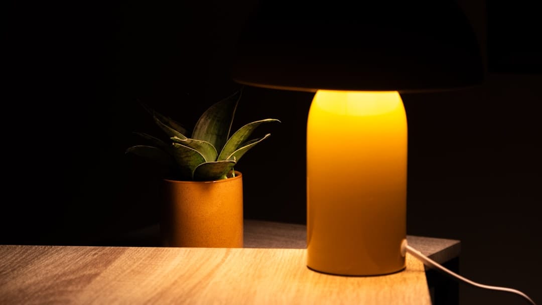 A yellow lamp and potted plant on a wooden table.